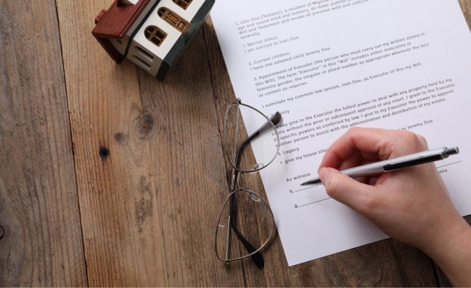 Person signing a will beside glasses and a model house